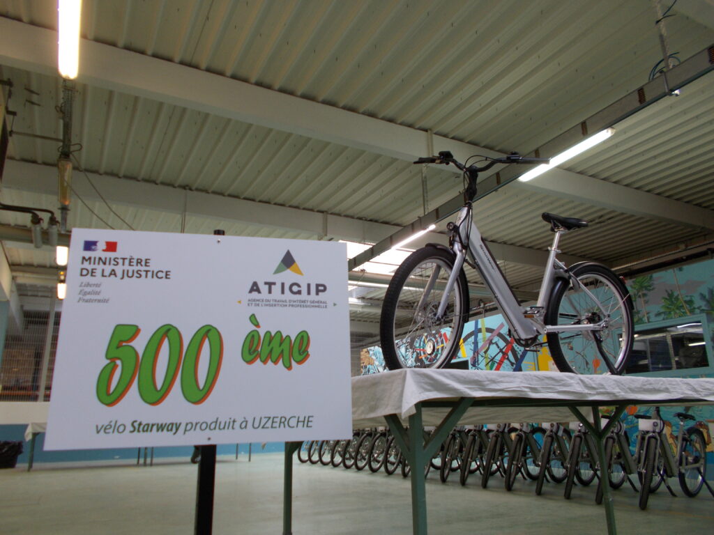 Photo dans un hangar d'un vélo à côté d'une pancarte "500ème"